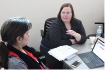 2 women sitting at a desk in front of a computer