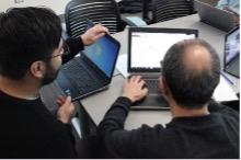 2 men sitting at a table together looking at a computer