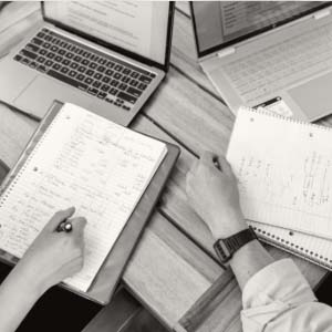 View looking down at 2 people's laptops and notebooks as they work