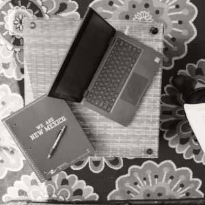 View looking down on an open laptop with a We Are New Mexico notebook sitting beside it