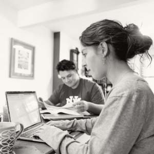 One person working on a laptop with another flipping through a textbook