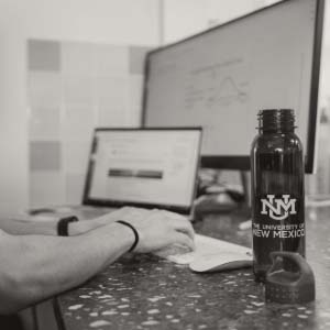 Red UNM water bottle sitting open on a table with someone working on a computer in the background