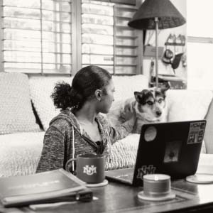 Girl petting her dog with open laptop in front of her