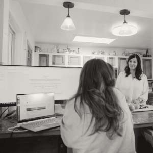 Two people talking while one works on a computer and another cuts fruit