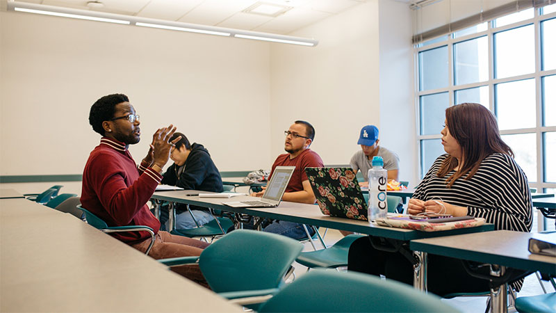 An instructor sitting down in front of the class lecturing